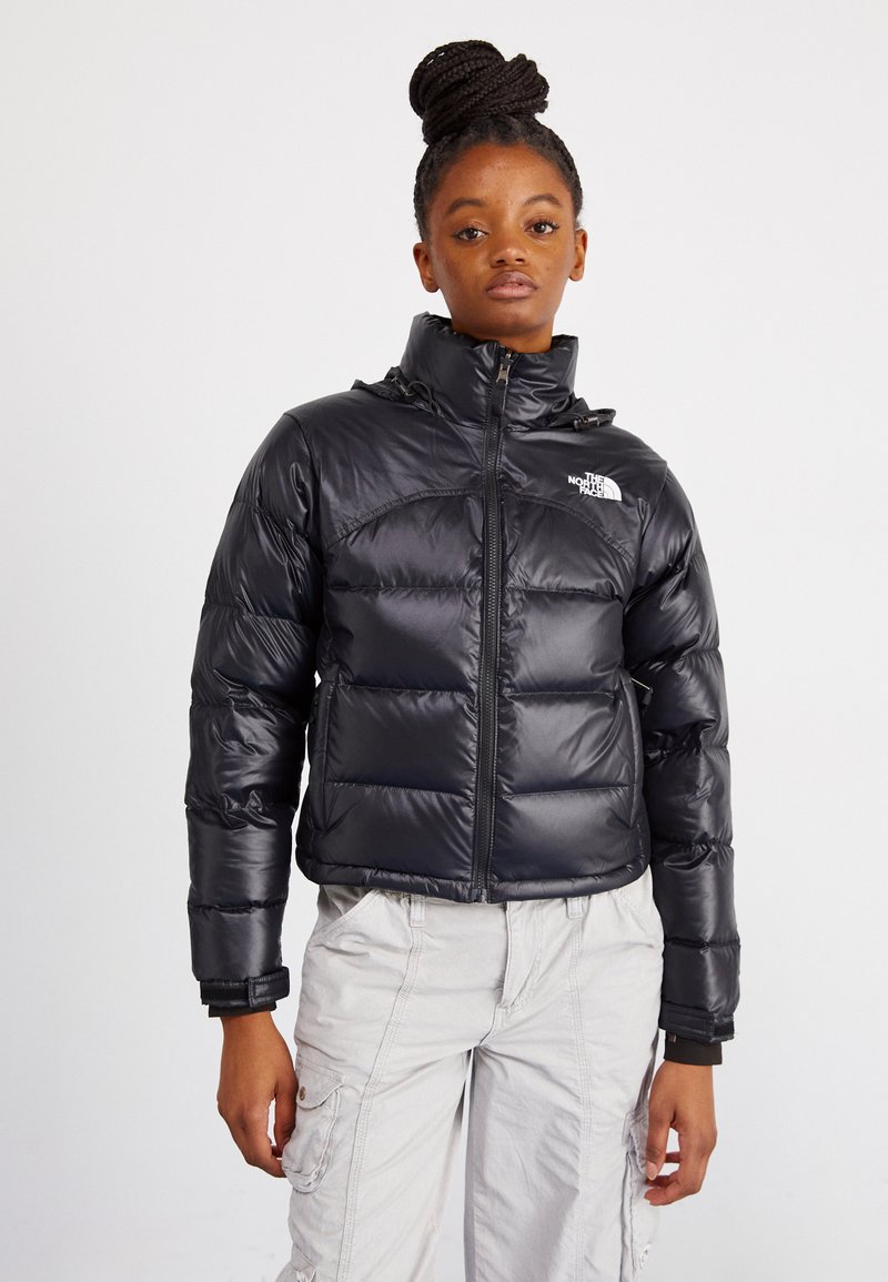 Črn puhasti plašč z sijočo površino, z visokim ovratnikom, sprednjim zadrgo in logotipom North Face na levem prsnem košu. Tekstuirana, prešita zasnova.