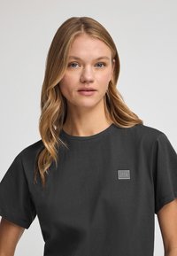 Svart bomullströja med rund halsringning och korta ärmar, med en liten fyrkantig logotyp på vänster bröst.