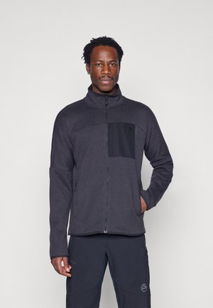 Ciemnoszara polarowa kurtka z wysokim kołnierzem, zamkiem z przodu oraz czarną kieszenią na piersi. Gładka faktura, z logo na kieszeni piersiowej.