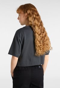 Grey cropped t-shirt with short sleeves. Cotton material. Smooth texture, round neckline. Black pants with back pockets visible in the image.
