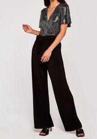 Pantalons larges noirs avec une ceinture à nouer, accompagnés d'un haut brillant en sequins argentés à manches courtes et à décolleté plongeant.