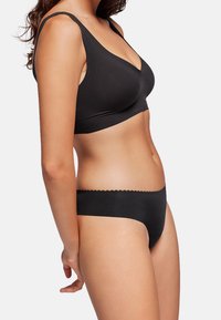 Sostenedor negro con un material suave y elástico y un escote en V profundo. Tanga negro a juego con bordes scalloped, diseño sin costuras y cobertura mínima.