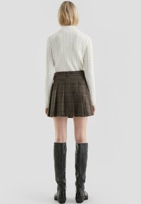 Sweter w splot bublu, kremowy, brązowa spódnica w kratkę z plisami mini oraz czarne skórzane kozaki do kolan. Gładkie faktury oraz dopasowany krój.