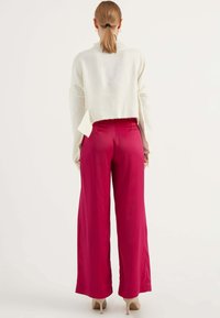 Witte, cropped trui met een gestructureerde afwerking, gecombineerd met wijde, hoge taille, glanzende roze broek en naakte hakken.