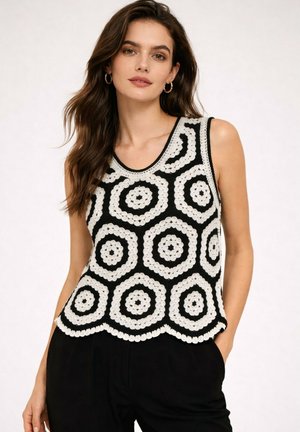 Femme portant un haut en tricot noir sans manches avec de grands motifs circulaires blancs en crochet, associé à un pantalon noir et des boucles d’oreilles créoles dorées.