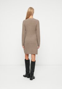 Sweter-dress w kolorze taupe, do kolan, z długimi rękawami i okrągłym dekoltem, w połączeniu z czarnymi, skórzanymi bootsami do kolan.