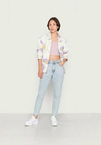 Casaco estampado floral em branco com flores roxas, combinado com um top cropped rosa claro, jeans azuis de cintura alta e sapatilhas brancas.