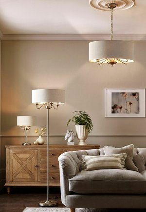 Beige living room with tufted sofa, striped pillow, wooden sideboard, table and floor lamps, potted plant, horse sculpture, and floral wall art.