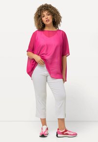 Haut rose transparent à manches courtes, associé à un pantalon blanc court et des baskets roses. La tenue combine un tissu léger et des couleurs vives.