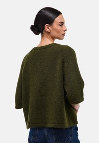 Pull en tricot vert olive à coupe décontractée, avec un col côtelé et des manches arrivant aux coudes. Texture douce avec une coupe légèrement oversize.