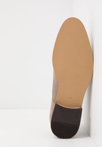 Beige Wildleder-Stiefelette mit glatter Oberfläche und einem dunklen Gummihighheel. Die Sohle ist beige mit einer leichten Textur. Größe markiert als 42.