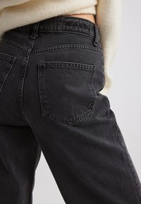 Mustad denim püksid kõrge vöökohaga, traditsiooniliste tagataskutega ja tekstureeritud kangaga, millel on peened õmblusdetailid.