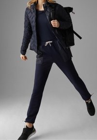 Námořnická prošívaná bunda se zipem, doplněná o námořnické tepláky s elastickým pasem a kapsami, které jsou kombinovány s černými teniskami.