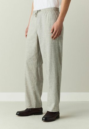 Person trägt hellgraue, strukturierte Hose mit elastischem Bund und Kordelzug, kombiniert mit dunkelbraunen Leder-Loafers.