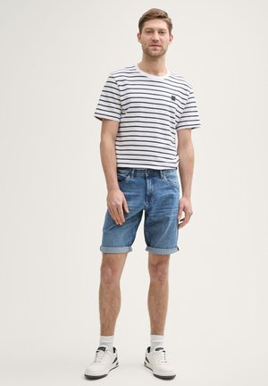 T-shirt à manches courtes rayé en blanc et bleu marine, associé à un short en jean à ourlet retroussé. Le mannequin porte des baskets blanches et des chaussettes de cheville.
