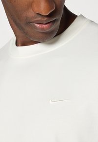 Sudadera blanca de Nike con cuello redondo y un sutil logo bordado en el pecho, hecha de una tela suave y lisa.