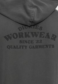 Hanorac gri cu glugă, care prezintă un imprimeu mare negru cu textul "Dickies Workwear Since '22 Quality Garments" scris cu litere îngroșate.