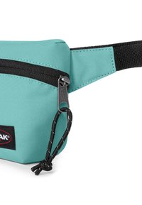 Sac banane en tissu turquoise avec une fermeture éclair noire, une sangle noire et un patch de marque. Présente un tirette de fermeture éclair noire proéminente et une surface texturée.