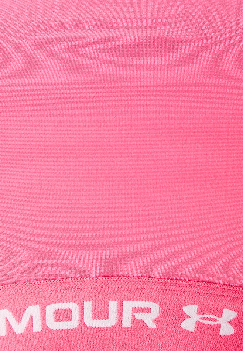 Reggiseno sportivo rosa aderente con una consistenza liscia, caratterizzato da un elastico bianco con testo e logo nella parte inferiore. Visuale ravvicinata.