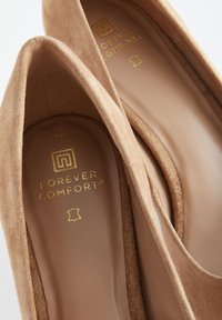 Tacchi beige in camoscio con punta arrotondata e fodera interna liscia. Marchio dorato "FOREVER COMFORT" impresso sulla soletta.