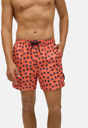 Bañadores cortos en color coral con patrón de peces en azul marino, cintura elástica y bolsillos frontales. Hechos de una tela ligera ideal para actividades acuáticas.