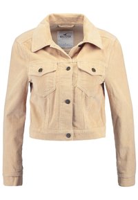 Veste en velours côtelé beige avec un col, deux poches poitrine et des fermetures à boutons. Tissu texturé, coupe courte et motif à côtes.