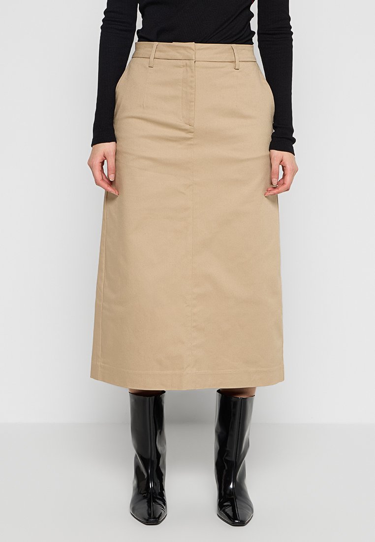Beżowa bawełniana spódnica midi z płaskim przodem, szlufkami na pasek i bocznymi kieszeniami. Noszona z czarnymi błyszczącymi kozakami za kolano. Prosta, prosta sylwetka.