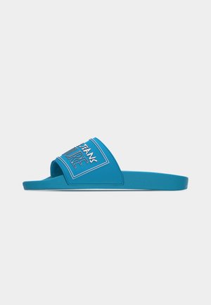 Μπλε σανδάλι με λαστιχένια σαγιονάρα, ανοιχτό δάκτυλο, φαρδιά λουρί με λευκή περίγραμμα κείμενο και σχέδιο, εμφανιζόμενο σε πλάγια όψη σε φωτεινό φόντο.