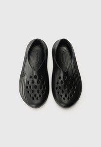 Black slip-on shoes with a smooth texture, featuring multiple ventilation holes and a rounded toe shape for breathability and comfort.