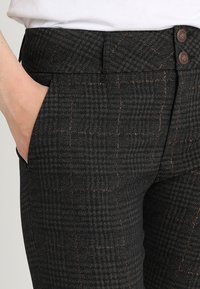 Svart rutiga byxor gjorda av texturerat tyg, med en figursydd design, sidofickor och två knappar framtill för stängning.