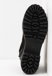 Zapato de ante negro con una suela de goma texturizada, que presenta un patrón de relieve profundo para mayor agarre. Talla marcada como 37 en la suela.