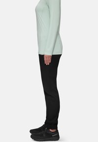 Lichtgroene lange mouwen top gecombineerd met zwarte taps toelopende broek en zwarte sportschoenen, wat een slanke, functionele sportieve uitstraling laat zien.