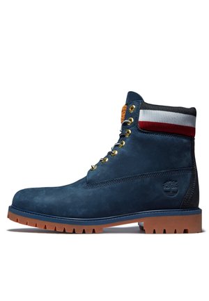 Granatowy skórzany botek na sznurowadła z brązową gumową podeszwą, złotymi oczkami i dzianinowym kołnierzem w paski czerwono-biało-czarne.