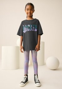 Čierne oversized tričko s nápisom "WICKED" z irizujúcich flitrov, skombinované s pastelovo irizujúcimi legínami a čiernymi vysokými teniskami.