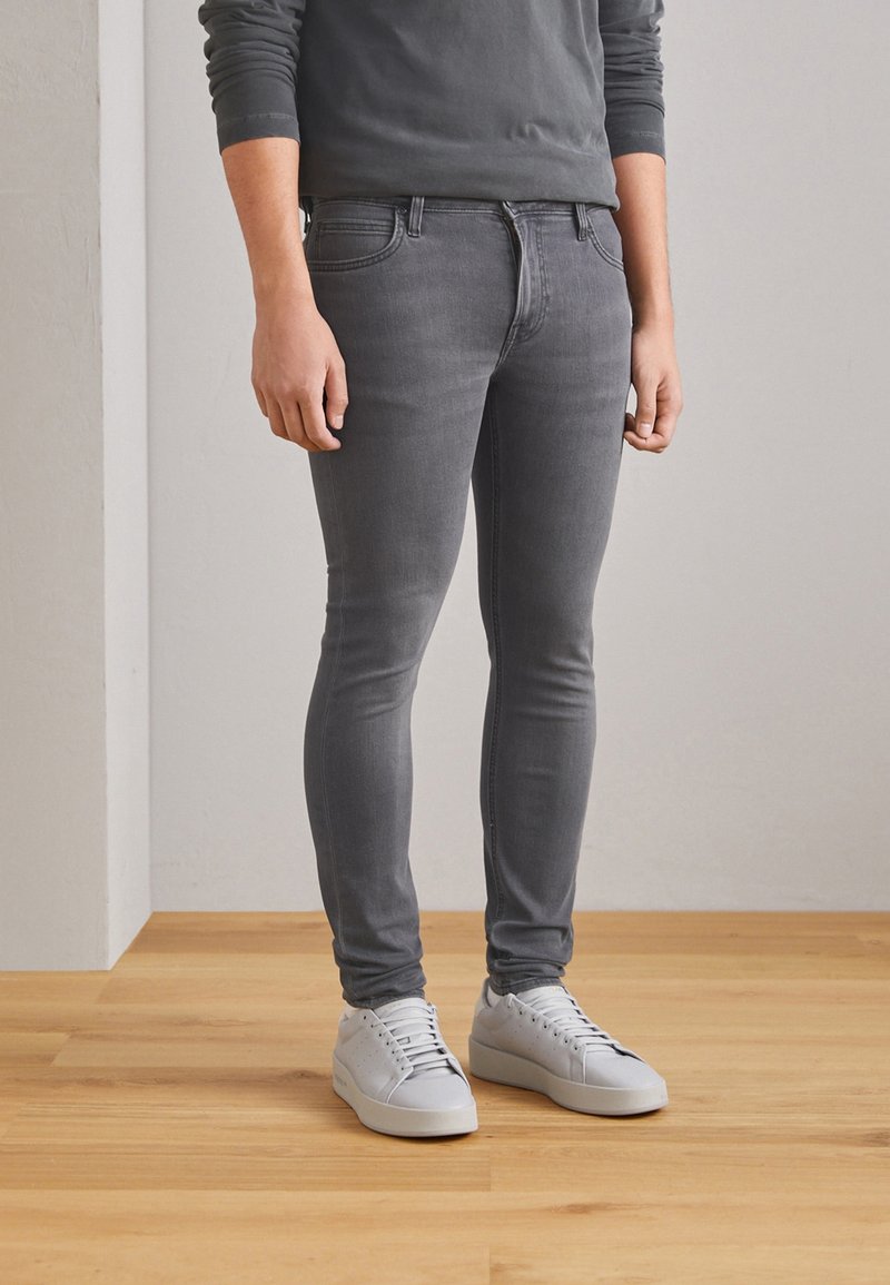 Jeans de denim gris de corte ajustado, con una textura suave, diseño de cinco bolsillos y un acabado sutilmente desgastado, combinados con zapatillas blancas.