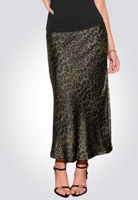 Jupe maxi en satin vert olive avec imprimé léopard noir. Texture lisse, légèrement évasée vers l'ourlet, portée avec des sandales noires à brides.