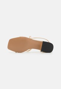 Sandale à talons avec des lanières, dotée d'une base nude, de lanières en or métallique et d'un talon en caoutchouc noir texturé. Semelle lisse, accents minimalistes.
