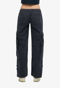 Mørkeblå cargo-bukser med elastisk talje, sidelommer og justerbare cuffs, lavet af letvægtsstof. Har et lille logo-patch.