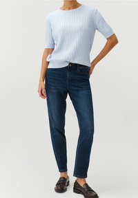 Maglione a coste di colore azzurro chiaro con maniche corte, abbinato a jeans high-waisted blu scuro e mocassini scuri. Texture morbida e vestibilità casual.