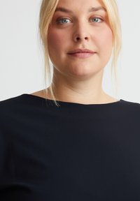 Dunkelblaues, kurzärmeliges Oberteil mit Bootsausschnitt, glatter Textur und minimaler Detailgestaltung. Lässige und figurbetonte Silhouette.
