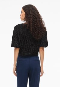 Melnas strukturētas blūzes ar īsām piedurknēm, kurai ir slāņota dizaina pieeja. Apvienota ar tumši ziliem biksēm, kas nodrošina brīvu piegulšanu un vienkāršu griezumu.