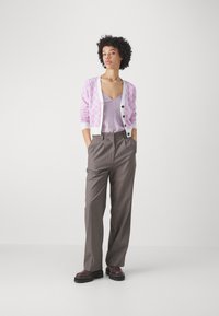 Cárdigan lila claro con patrón de espiga, combinado con una blusa sin mangas lavanda y pantalones de tiro alto grises; zapatos de plataforma negros.