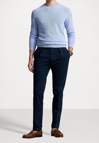 Světlomodrý pletený svetr, tmavě modré plisované kalhoty a hnědé kožené společenské boty. Svetr má kulat ý výstřih; kalhoty jsou na míru.