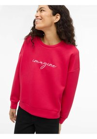 Rød genser laget av mykt stoff med rund hals og avslappet passform. Dekorativ "imagine" brodert i hvitt over brystet.