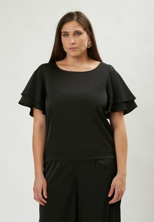 Top nero realizzato in tessuto morbido con scollatura rotonda e maniche corte a volant sovrapposte. Presenta una vestibilità comoda, abbinato a pantaloni neri.