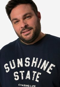 Námořnická modrá mikina s texturovaným bílým grafickým nápisem "SUNSHINE STATE" a "CHASING LIFE" v přední části; žebrovaný límec a manžety.