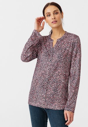 Langarmbluse mit V-Ausschnitt, ausgestattet mit einem abstrakten Drehmuster in Rot, Weiß und Marineblau auf leichtem, strukturiertem Stoff.