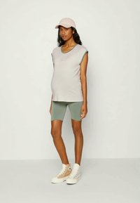 Top de maternidade às riscas cinza e brancas, calções de bicicleta verdes, boné rosa, ténis em creme. Conjunto casual com design descontraído e texturas suaves.