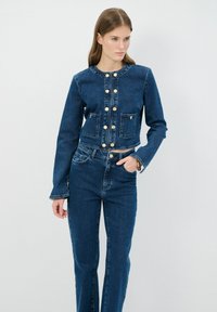 Chaqueta de denim y jeans de tiro alto a juego, ambos en azul oscuro, con botones dorados y dos bolsillos frontales. Textura lisa, diseño corto.