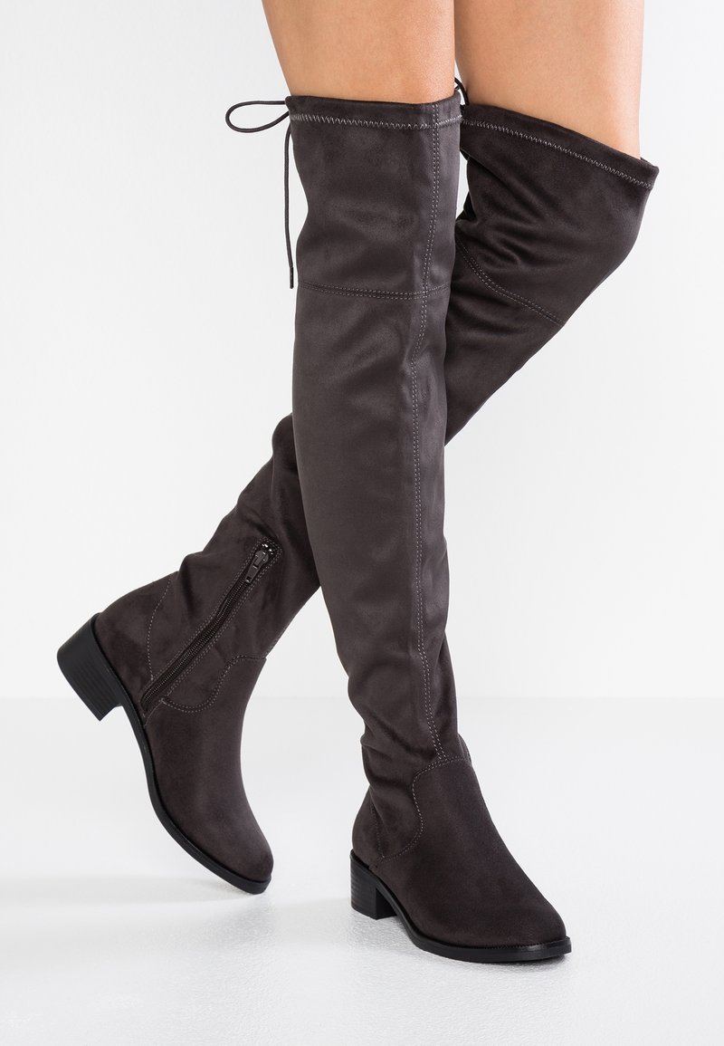 Botas por encima de la rodilla en ante gris oscuro con un acabado texturizado, punta cuadrada y cremallera lateral. Presenta un lazo ajustable en la parte superior.